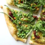 A fresh mix of flavors and veggies comes together with this Spring Greens Pesto Pizza. A crunchy crust, fresh pesto, sun-dried tomatoes, chickpeas, asparagus, peas and arugula make a light vegan pizza! | ThisSavoryVegan.com #vegan #veganpizza