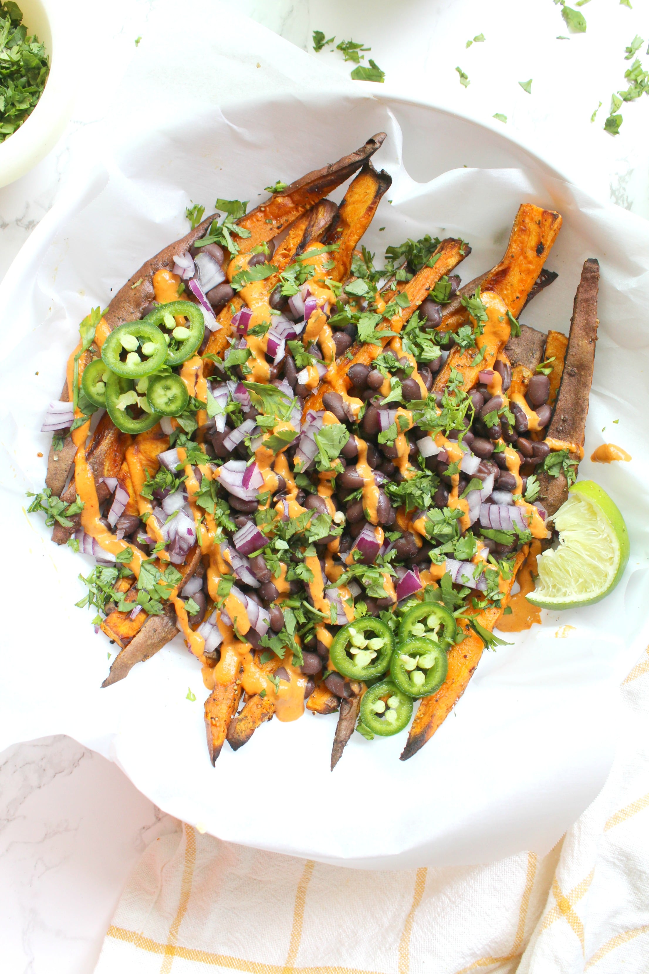 These Loaded Sweet Potato Fries with Vegan Chipotle Sauce are the perfect party snack. Sweet potato fries are baked until crispy then topped with beans, red onion, cilantro and a spicy chipotle tahini sauce | ThisSavoryVegan.com #thissavoryvegan #loadedfries #vegan