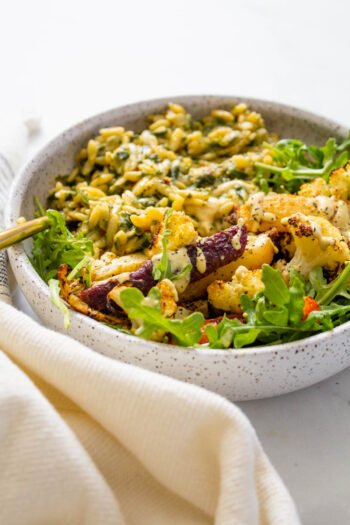 These Roasted Veggies with Creamy Vegan Spinach Orzo make up the ultimate bowl. Topped off with Mustard Tahini Dressing and fresh arugula! | ThisSavoryVegan.com #thissavoryvegan #veganbowls #spinachorzo