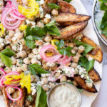These Loaded Greek Potato Wedges are a great vegan meal idea. Marinated chickpeas, vegan feta, crispy potato wedges & a tahini sauce | ThisSavoryVegan.com