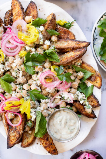 These Loaded Greek Potato Wedges are a great vegan meal idea. Marinated chickpeas, vegan feta, crispy potato wedges & a tahini sauce | ThisSavoryVegan.com