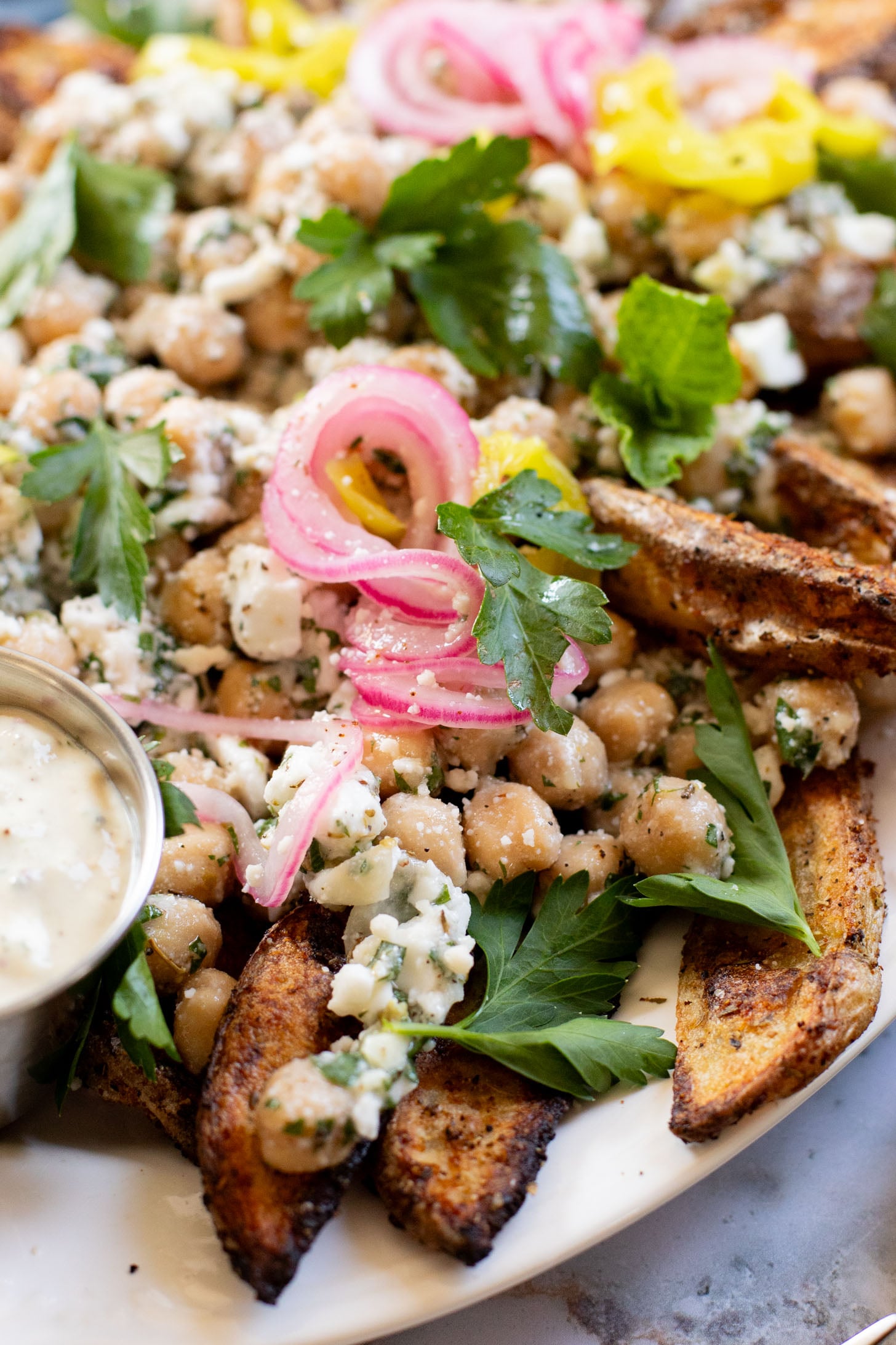 These Loaded Greek Potato Wedges are a great vegan meal idea. Marinated chickpeas, vegan feta, crispy potato wedges & a tahini sauce | ThisSavoryVegan.com
