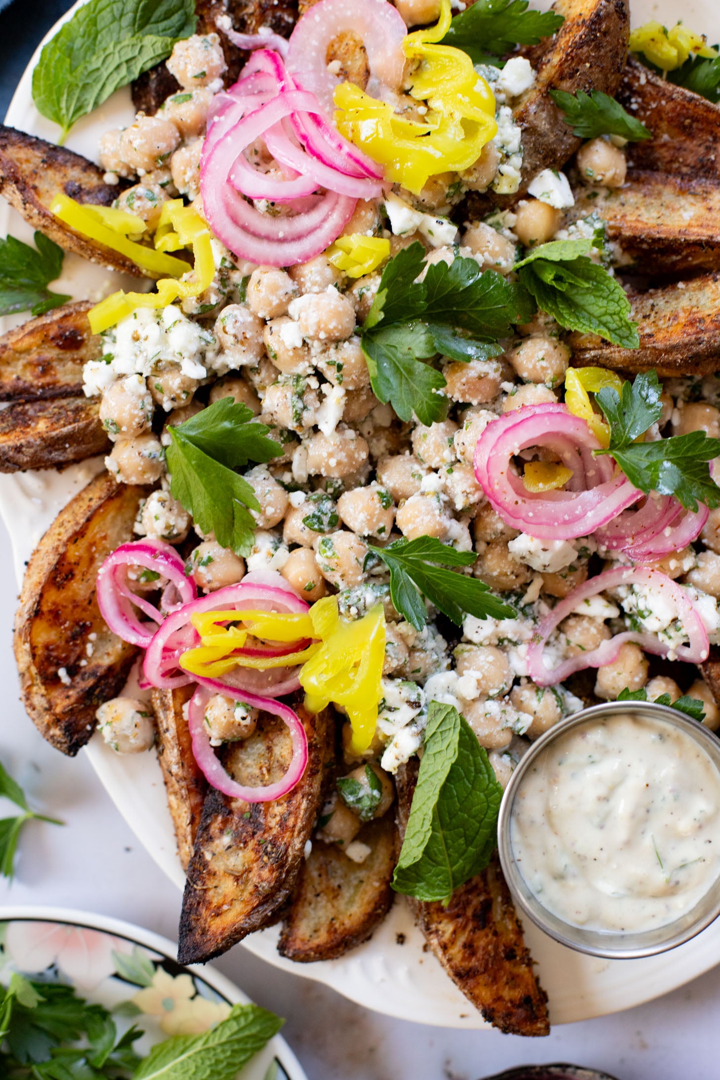 These Loaded Greek Potato Wedges are a great vegan meal idea. Marinated chickpeas, vegan feta, crispy potato wedges & a tahini sauce | ThisSavoryVegan.com