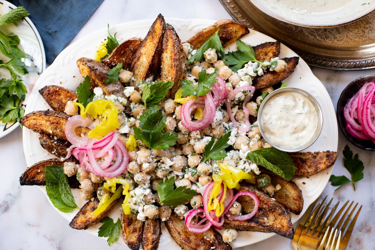 These Loaded Greek Potato Wedges are a great vegan meal idea. Marinated chickpeas, vegan feta, crispy potato wedges & a tahini sauce | ThisSavoryVegan.com