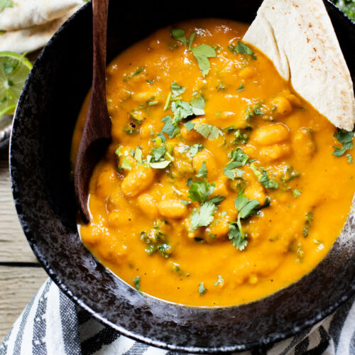 This Curried White Beans & Kale recipe is cozy and veggie packed! Beans are simmered in a coconut & squash sauce to make a delicious vegan curry | ThisSavoryVegan.com